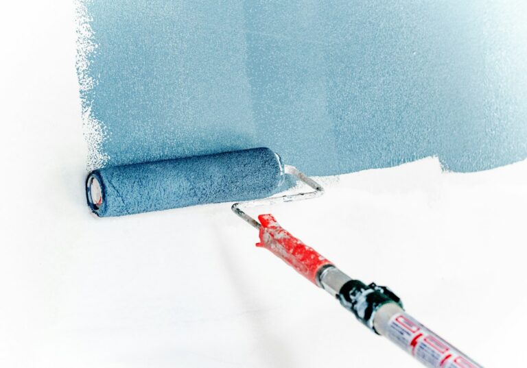 A roller applying blue paint to a white wall